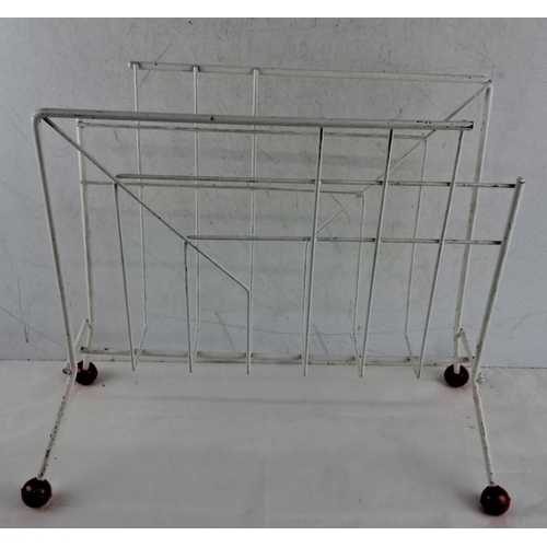 676 - This is a Mid-Century Modern white metal magazine rack on red caster wheels, featuring a geometric d... 