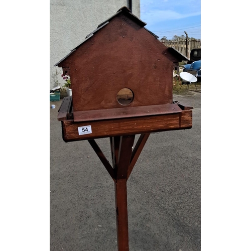 54 - Wooden birdhouse with a sturdy stand, featuring a pitched roof and circular entry holes on both side... 