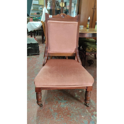 457 - Victorian upholstered mahogany armchair features a carved backrest and turned front legs with caster... 