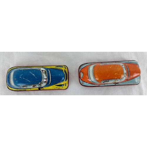 13 - Pair of vintage tin lithograph toy cars with vibrant graphics depicting passengers inside.