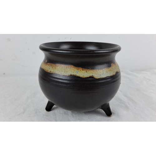 127 - Black pottery vessel with a tripod base, featuring a rustic glaze band. Mark inscribed on the bottom... 