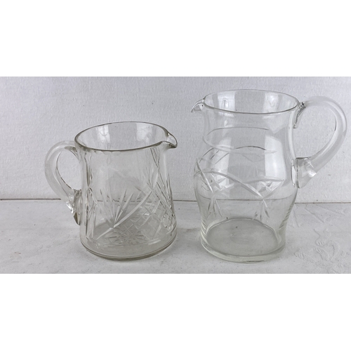 86 - Two vintage cut glass etched pitchers featuring geometric and foliage designs.