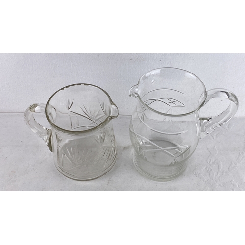 86 - Two vintage cut glass etched pitchers featuring geometric and foliage designs.