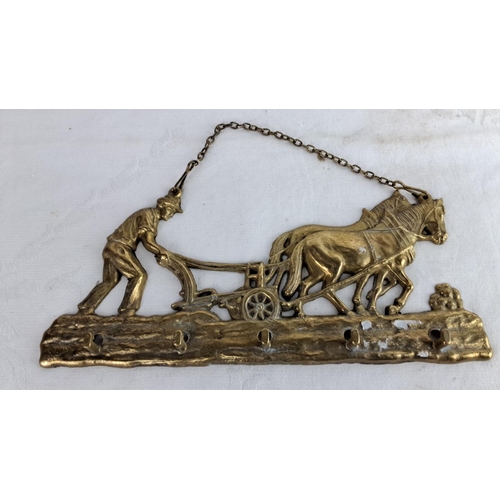 121 - Brass wall hanging of a farmer plowing with horses. Features chain for hanging.