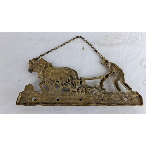 121 - Brass wall hanging of a farmer plowing with horses. Features chain for hanging.