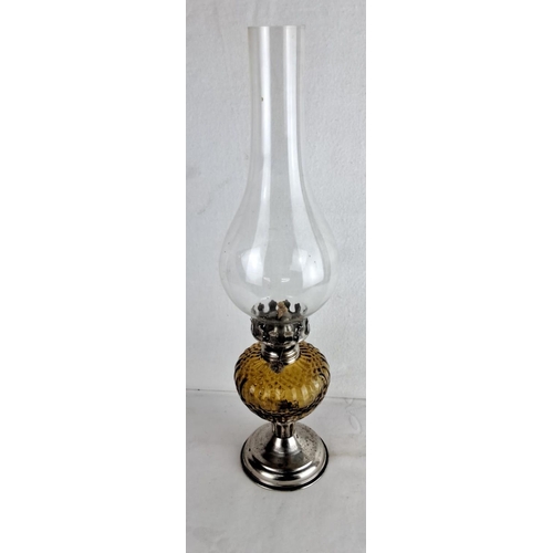 122 - Amber glass oil lamp features a clear glass chimney and metal base. It includes an intricately desig... 