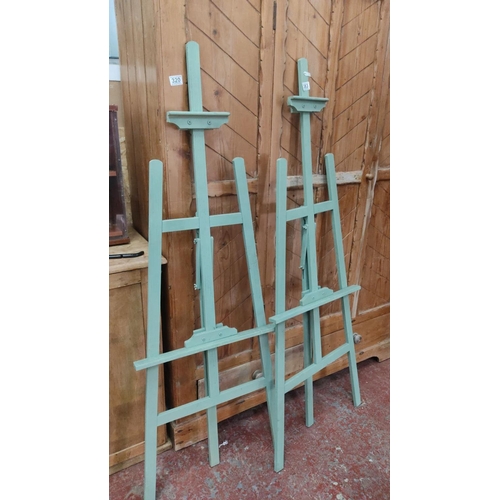 383 - Pair of adjustable wooden artist easels, painted in mint green, featuring shelf supports.