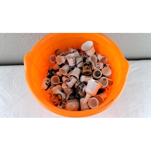 24 - Collection of ceramic souvenir thimbles, housed in a Halloween-themed orange plastic bucket. Assorte... 