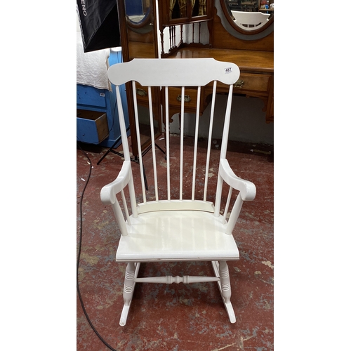 487 - White wooden rocking chair featuring spindled back and armrests. Classic design.