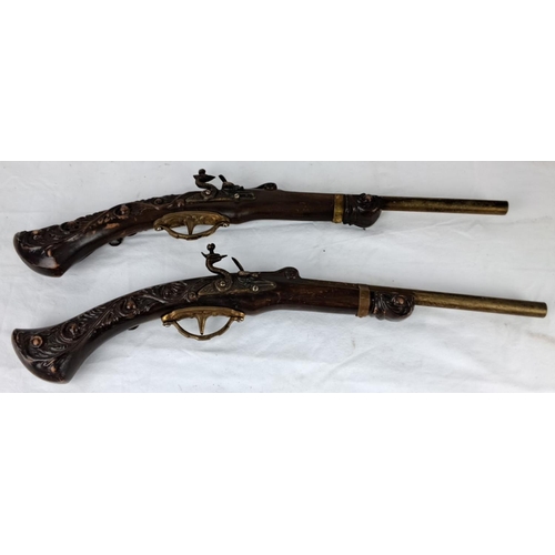 59 - Pair of  replica flintlock pistols feature intricately carved wooden stocks and brass detailing.