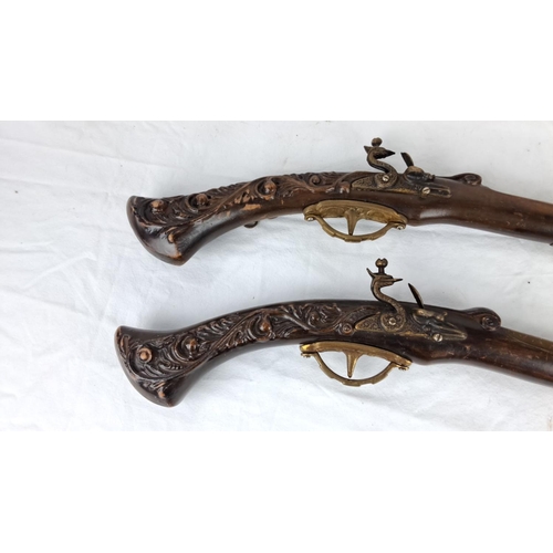 59 - Pair of  replica flintlock pistols feature intricately carved wooden stocks and brass detailing.