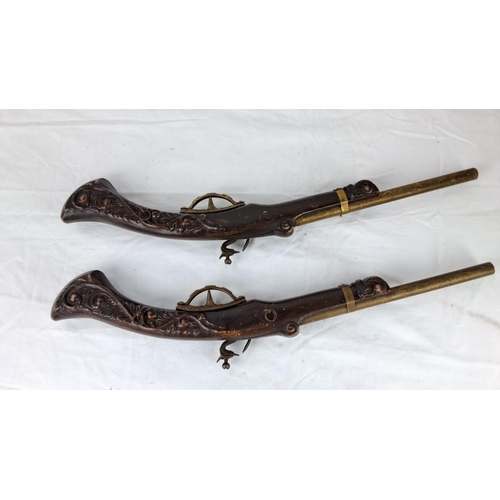 59 - Pair of  replica flintlock pistols feature intricately carved wooden stocks and brass detailing.