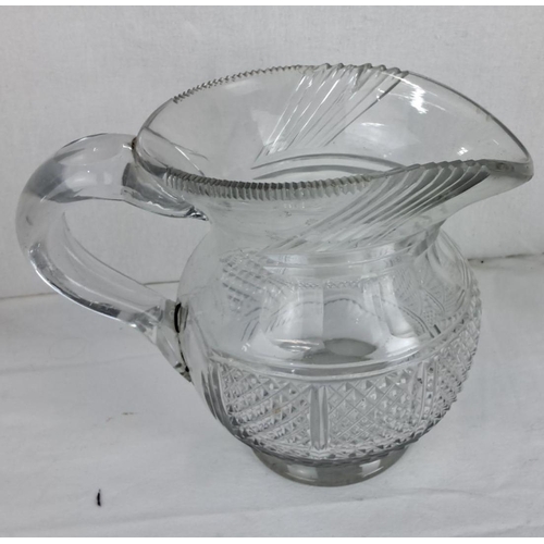 83 - Cut glass pitcher with a curved handle, intricate diamond and linear patterns, and a scalloped rim.