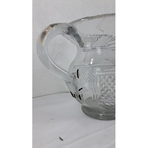 83 - Cut glass pitcher with a curved handle, intricate diamond and linear patterns, and a scalloped rim.