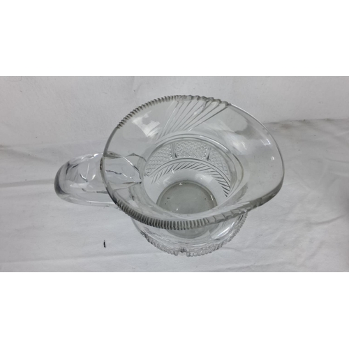 83 - Cut glass pitcher with a curved handle, intricate diamond and linear patterns, and a scalloped rim.