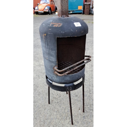 37 - Repurposed metal chiminea with grill, featuring a cylindrical design and elevated on sturdy legs.