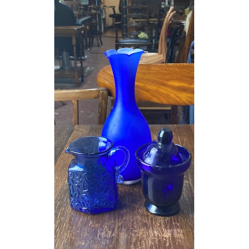 312 - Collection of three cobalt blue glassware pieces, including a vase, textured pitcher, and lidded jar... 