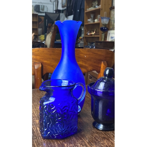 312 - Collection of three cobalt blue glassware pieces, including a vase, textured pitcher, and lidded jar... 