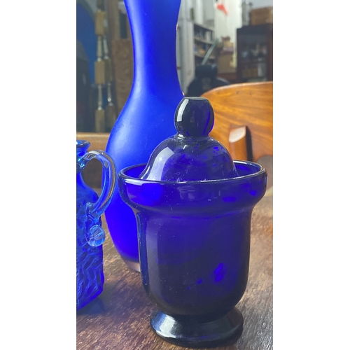 312 - Collection of three cobalt blue glassware pieces, including a vase, textured pitcher, and lidded jar... 