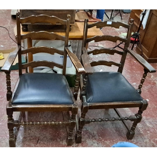 555 - Pair of wooden ladder-back armchairs with turned legs and black upholstered seats, rustic design.