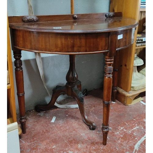 423 - Mahogany demi-lune side table with carved details and elegantly turned legs, featuring a central ped... 