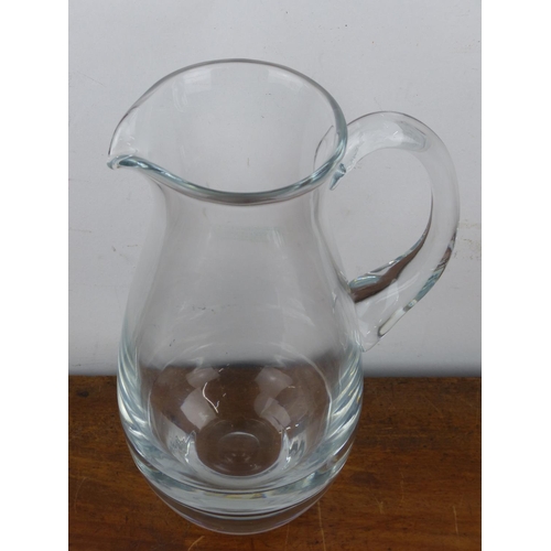 147 - A large & heavy glass jug, measuring 27cm tall.