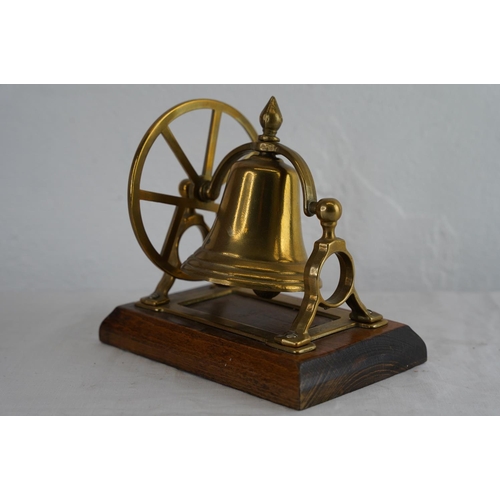 215 - A small mounted brass fire bell on an oak plinth, measuring 11.5cm x 18cm.