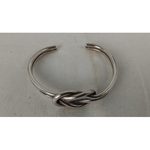 182 - A Mexican sterling silver open bangle, of rounded wire form with a central knot motif; stamped “925”... 
