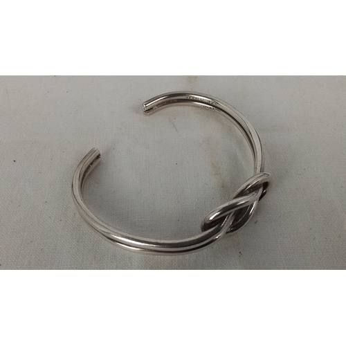 182 - A Mexican sterling silver open bangle, of rounded wire form with a central knot motif; stamped “925”... 