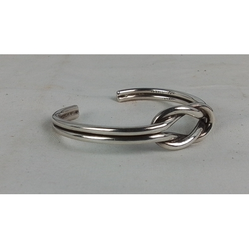 182 - A Mexican sterling silver open bangle, of rounded wire form with a central knot motif; stamped “925”... 