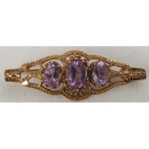 354 - A gold brooch of openwork form, set with three oval-cut purple stones, the central stone larger; fit... 