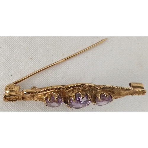 354 - A gold brooch of openwork form, set with three oval-cut purple stones, the central stone larger; fit... 