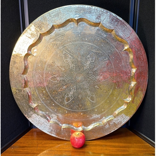 32 - A large circular Middle Eastern style metal tray or charger, with scalloped rim and densely chased f... 