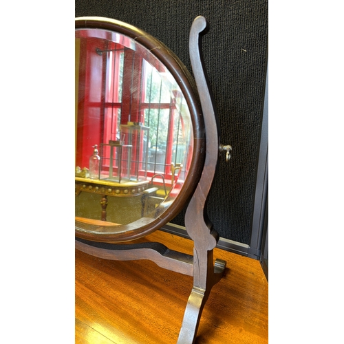 8 - An oval mahogany dressing mirror, the bevelled plate within a swivelling frame, raised on a shaped s... 