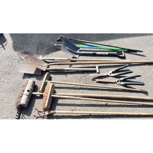 29 - A mixed group of garden tools comprising rakes, spades, shovels, forks, brooms, hoes, a three-prong ... 