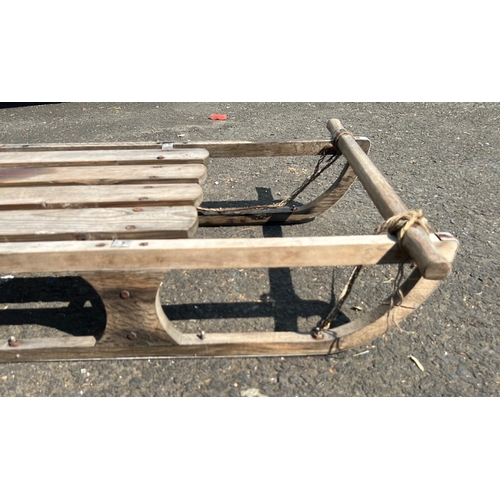 24 - Wooden snow sled with slatted platform and curved runners, fitted with a transverse handlebar and ro... 