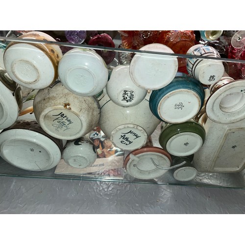 257 - TWO SHELVES OF JERSEY POTTERY INCLUDING QUARTZ WALL CLOCKS, VASES, ROSE BOWLS, ETC