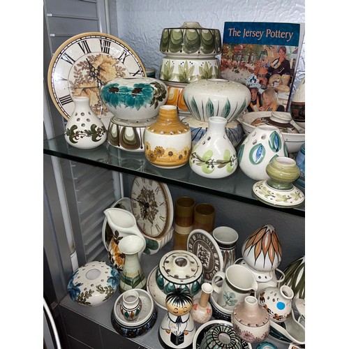 257 - TWO SHELVES OF JERSEY POTTERY INCLUDING QUARTZ WALL CLOCKS, VASES, ROSE BOWLS, ETC