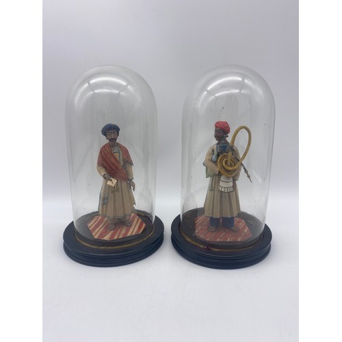 368 - TWO INDIAN PAPER FIGURES UNDER GLASS DOMES ONE CARRYING HOOKAH PIPE AND ROLLED RUG, THE OTHER WITH A... 