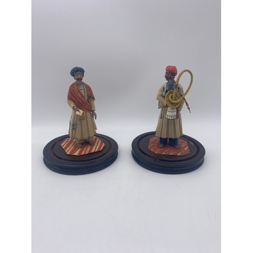 368 - TWO INDIAN PAPER FIGURES UNDER GLASS DOMES ONE CARRYING HOOKAH PIPE AND ROLLED RUG, THE OTHER WITH A... 