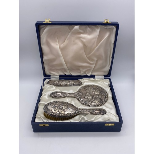 367 - CASED BIRMINGHAM SILVER BACKED REPOUSSE CHERUB VANITY SET INC. HAIR BRUSH AND HAND MIRROR