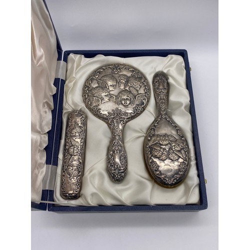 367 - CASED BIRMINGHAM SILVER BACKED REPOUSSE CHERUB VANITY SET INC. HAIR BRUSH AND HAND MIRROR