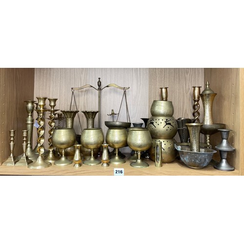 216 - SHELF OF PAIRS OF BRASS CANDLE STICKS, EASTERN INSPIRED VASE AND GOBLETS AND PAN SCALES