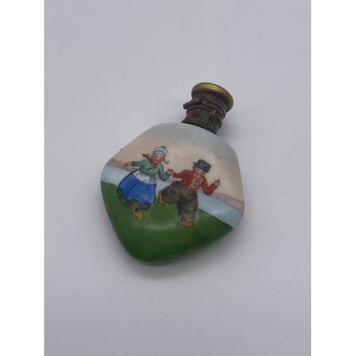 226 - THREE PORCELAIN BASE METAL TOPPED CYLINDRICAL AND SHAPED SCENT PHIALS WITH DUTCH BOY AND GIRL DECORA... 