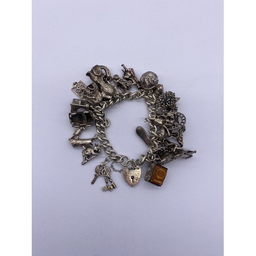 585 - SILVER CHARM BRACELET WITH HEART PADLOCK AND NUMEROUS NOVELTY CHARMS 91G APPROX