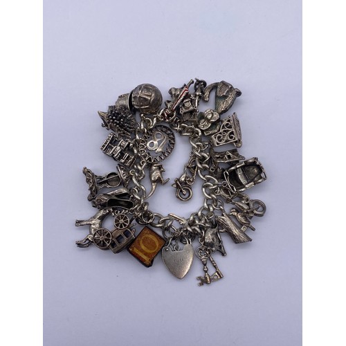 585 - SILVER CHARM BRACELET WITH HEART PADLOCK AND NUMEROUS NOVELTY CHARMS 91G APPROX