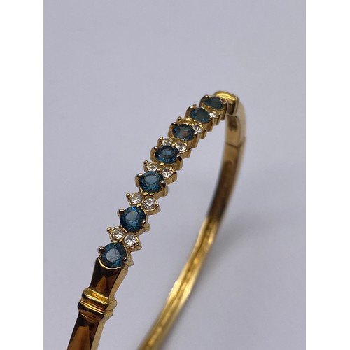 714 - UNMARKED YELLOW METAL CZ AND BLUE STONE BANGLE