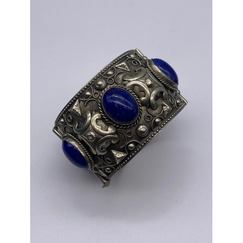 693 - ETHNIC WHITE METAL AND BLUE CABOCHON CUFF BANGLE AND A SILVER CROSS ON TRACE CHAIN