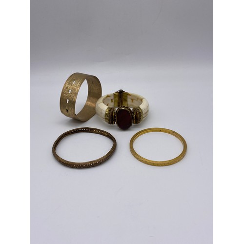 690 - THREE PLATED AND GOLD TONE COLOURED BANGLES (INC. BADEN EXAMPLE) AND AN ORNATE BONE BANGLE WITH RED ... 