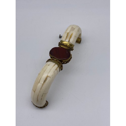 690 - THREE PLATED AND GOLD TONE COLOURED BANGLES (INC. BADEN EXAMPLE) AND AN ORNATE BONE BANGLE WITH RED ... 